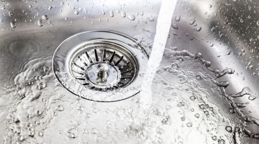 Stainless steel sink with flowing water, showcasing cleanliness for Maxwell-White Plumbing services.
