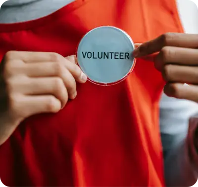 Person wearing an orange apron holding a badge that reads "VOLUNTEER," symbolizing community involvement in Maxwell-White Plumbing's food drive.