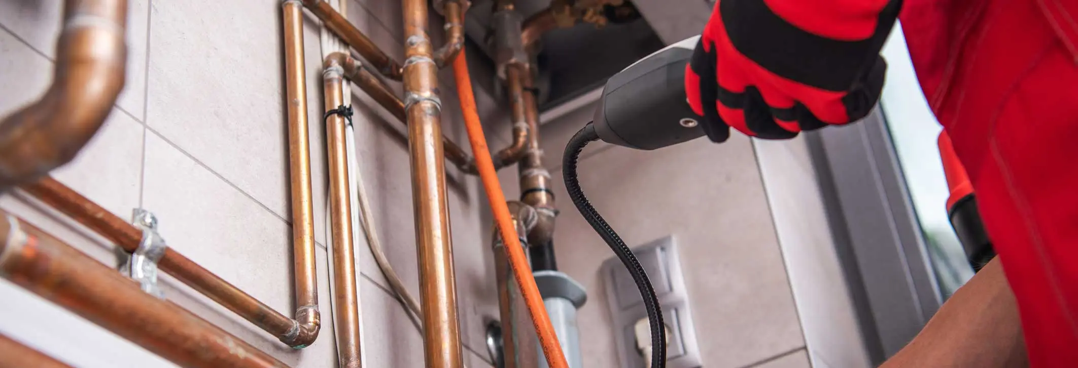 Plumber using gas leak detection equipment on copper pipes in a residential setting, highlighting Maxwell-White Plumbing's gas leak detection services for home safety.