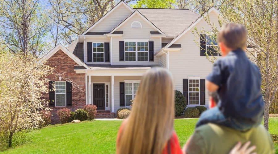 Woman carries child in front of a suburban house, highlighting family life relevant to Maxwell-White Plumbing's services.
