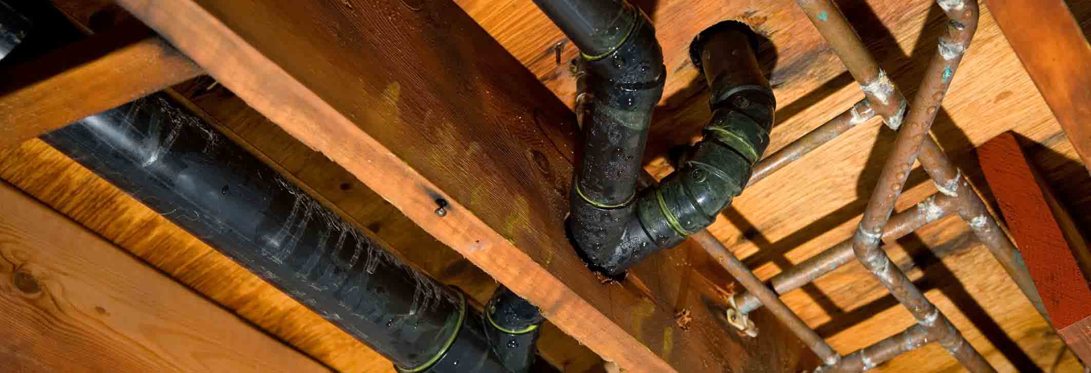 Pipes and plumbing under wooden flooring, illustrating potential slab leak issues relevant to Maxwell-White Plumbing's repair services in La Crosse, WI.