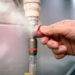 Hand fixing a plumbing fitting with steam escaping, showing a plumbing connector and rubber gasket by Maxwell-White Plumbing.