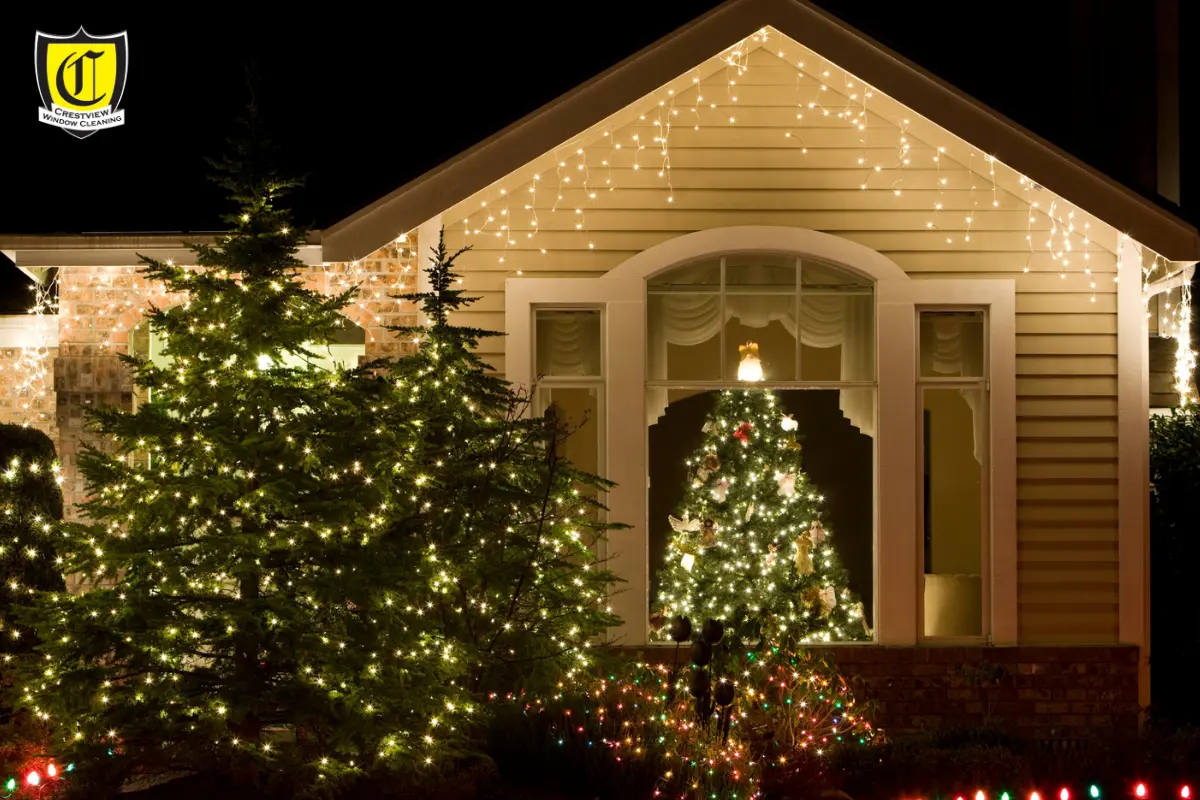 Professional installer placing warm gold and white Christmas lights on a suburban home at dusk, with glowing reflections on clean windows, showcasing Crestview’s festive and high-quality outdoor installation service.