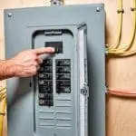 Hand adjusting a circuit breaker in an electrical panel, emphasizing the importance of electrical safety and panel upgrades for homes over 30 years old.