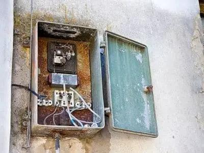 Old, rusty electrical panel with open cover, showing outdated wiring and components, indicating the need for electrical panel replacement for safety and modern standards.