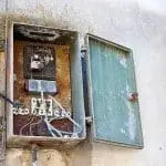 Old, rusty electrical panel with open door, showing worn wiring and components, illustrating the need for electrical panel upgrades for safety and reliability.