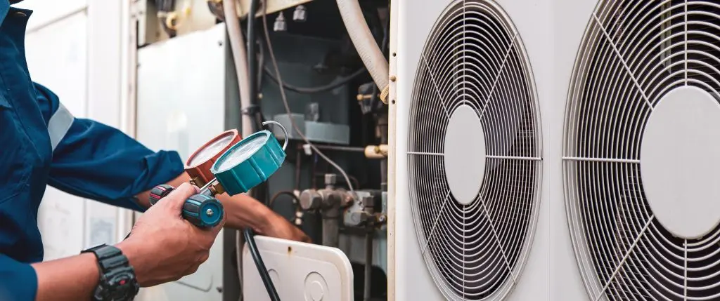 Heat and Air Conditioning, HVAC system service technician using measuring manifold gauge checking refrigerant and filling industrial air conditioner after duct cleaning maintenance outdoor compressor.