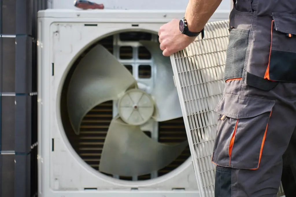 hvac maintenance plan Technician removing front cover grille from outdoor heat pump unit during residential HVAC service. Concept of heat pump maintenance, repair and home heating and cooling