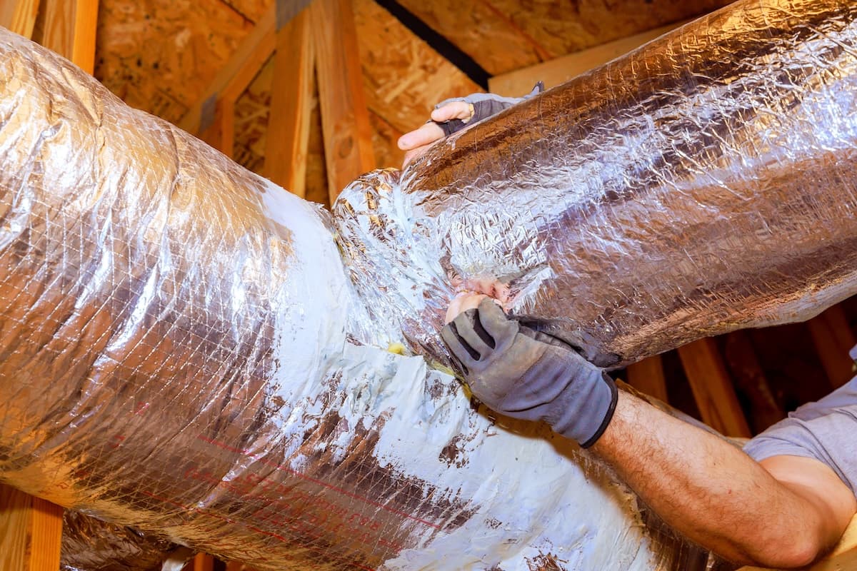 Workers are sealing duct connections in attic to ensure proper airflow, energy efficiency at home.