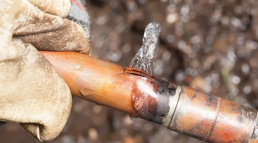 Close-up of a leaking copper water pipe with water dripping, illustrating a common plumbing issue relevant to water leak detection and repair services.