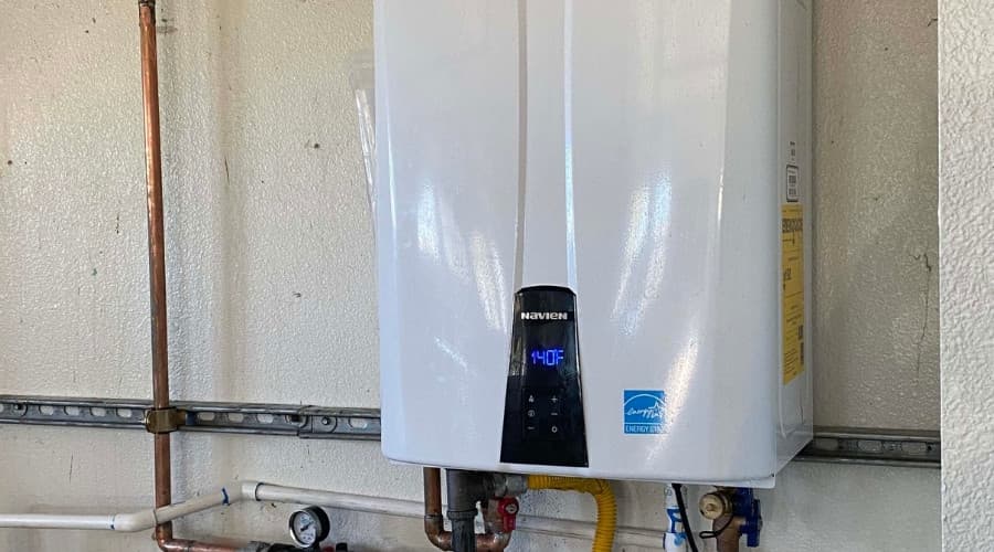 Tankless water heater mounted on a wall, featuring a digital display and plumbing connections, illustrating energy-efficient hot water solution for homeowners.