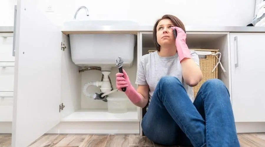 Woman with pink rubber gloves holds a wrench by a modern kitchen sink, addressing a plumbing issue for Scott Plumbing.