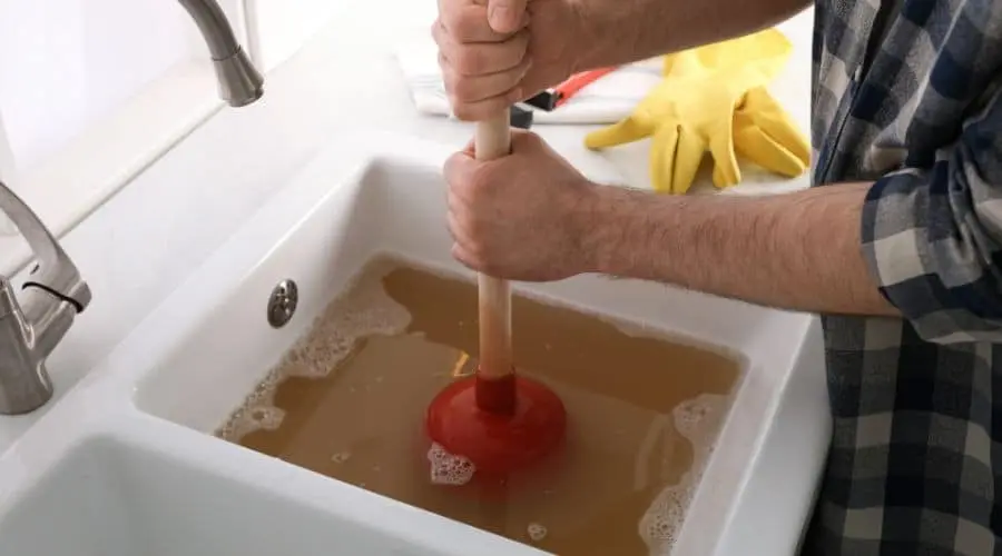 Person using a plunger to clear a clogged sink, illustrating common plumbing issues homeowners may face during the holiday season.