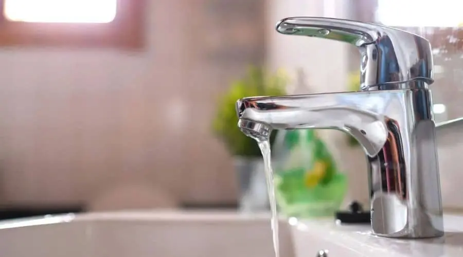 Shiny modern faucet over a sink with running water, showcasing plumbing solutions for sewer line issues by Scott Plumbing.