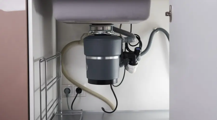 Kitchen garbage disposal unit installed under a sink, showcasing plumbing connections and electrical wiring, relevant to plumbing repair and maintenance services offered by Scott Plumbing.