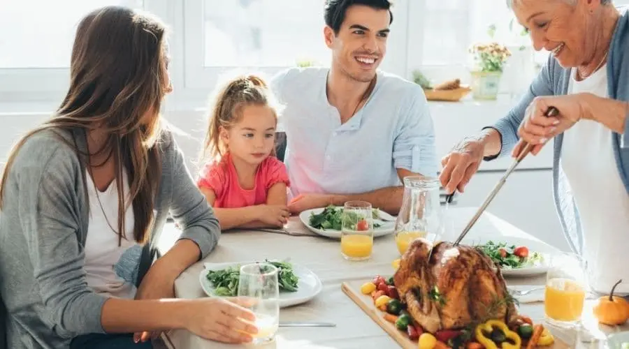 Four people at a dining table with roasted turkey, salads, and orange juice, showcasing a family gathering.