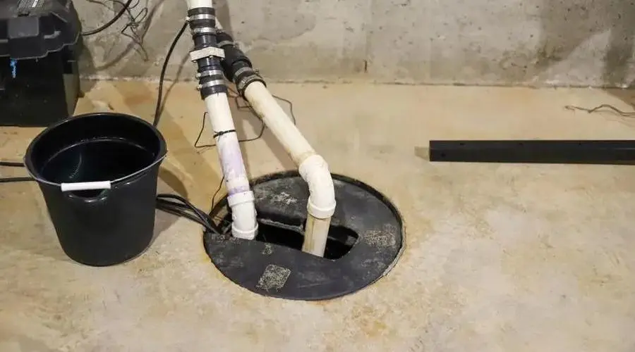 Sump pump system and water collection bucket on a concrete floor, showcasing plumbing maintenance by Scott Plumbing.