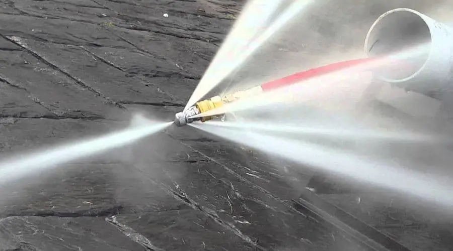 High-pressure water hose nozzle spraying on concrete, demonstrating plumbing service capabilities by Scott Plumbing.