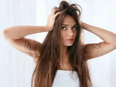 Woman with long, unkempt hair expressing frustration, representing the effects of hard water on hair quality and appearance.