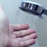 Close-up of modern showerhead with water stream and hand, illustrating plumbing fixtures by Quahog Plumbing.