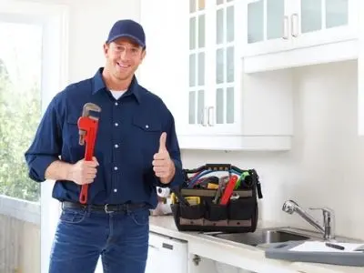 Professional plumber holding a wrench and giving a thumbs up, standing in a kitchen with a toolbox, illustrating plumbing expertise for slab leak repair and maintenance.