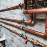 Copper pipes and fittings on textured wall, reflecting Quahog Plumbing's expertise in plumbing solutions.