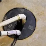 PVC plumbing pipes extending into a gray circular hole in a concrete surface for drainage by Quahog Plumbing.