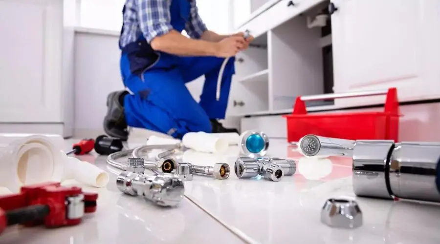 Plumber fixing a kitchen sink with tools and a red toolbox, showcasing Quahog Plumbing's professional services.