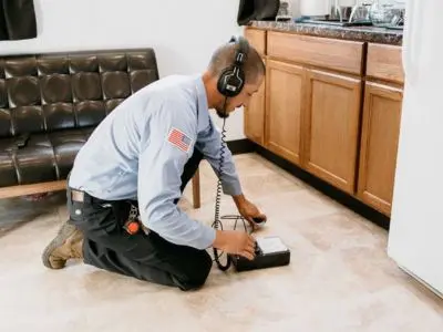 Professional plumber using acoustic leak detection equipment to locate water leaks in a residential kitchen.