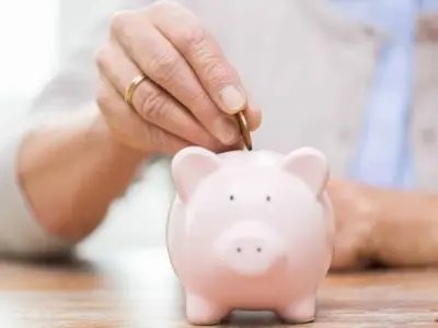 Hand inserting a coin into a pink piggy bank, symbolizing savings and financial planning for home maintenance costs, including water heater upkeep.