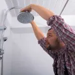 Man adjusting a modern showerhead, focused on plumbing maintenance for Quahog Plumbing services.