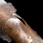 Damaged metal pipe with crack and frost, indicating plumbing deterioration near garbage disposal systems.