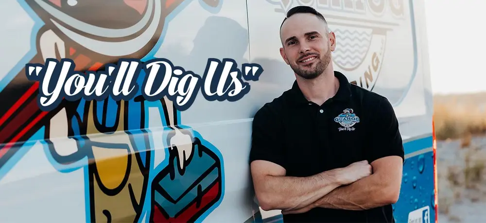 Man in black Quahog Plumbing shirt standing next to branded van with "You'll Dig Us" slogan, representing reliable plumbing services in Dighton, MA.