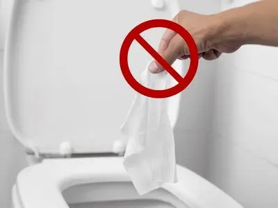 Hand holding a tissue above a toilet with a red "no" symbol, illustrating items that should not be flushed to prevent toilet clogs.