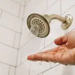 A hand is held under a shower head with very low water pressure, only a few streams of water are coming out.