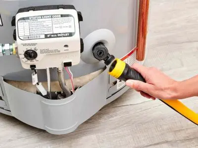 Person connecting a hose to a water heater for maintenance, showcasing the status light and plumbing components, emphasizing the importance of professional water heater servicing.