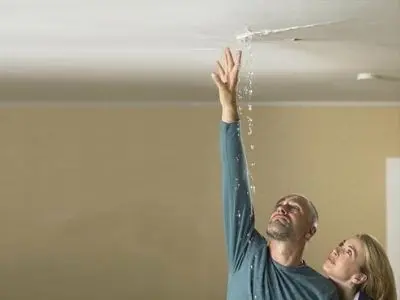 Man and woman observing water leak from ceiling, indicating plumbing issues related to hidden leaks and low water pressure in home plumbing systems.