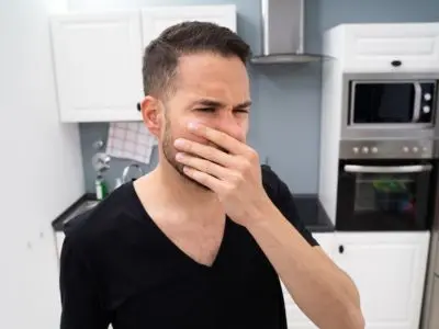 Man in a kitchen covering his nose, reacting to a bad odor, indicating potential signs of a gas leak.