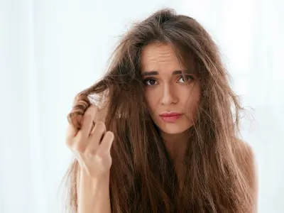 Woman with frizzy, unmanageable hair, looking concerned, illustrating effects of hard water on hair quality.