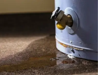 Leaking water heater with visible water pooling on the floor, highlighting potential corrosion and maintenance issues related to water heater systems.