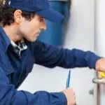 Male technician in work uniform repairing plumbing fixture with tools indoors for Quahog Plumbing services.