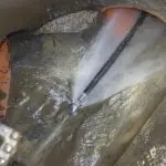 Jet of water spraying from a hose in an industrial setting, highlighting plumbing maintenance at Quahog Plumbing.