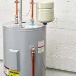 Water heater by Quahog Plumbing, metallic gray cylinder with copper pipes and safety labels.