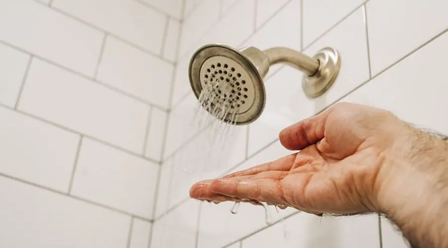 A hand is held under a shower head with very low water pressure, only a few streams of water are coming out.