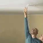 A man in a blue shirt and a woman with dark hair investigate water droplets from the ceiling, highlighting a plumbing issue.