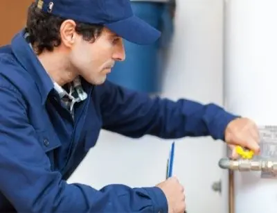 Plumber inspecting a water heater, checking valves and taking notes during maintenance to prevent system malfunction and leaks.