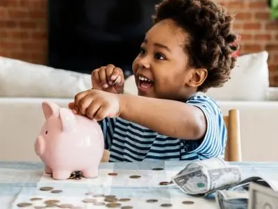 Child joyfully saving coins in a piggy bank, emphasizing financial savings and smart budgeting related to home water filtration systems.
