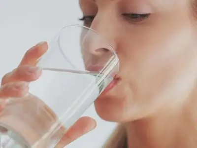 Woman drinking filtered water from a glass, highlighting the benefits of improved taste and safety of water filtration systems.