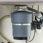 Garbage disposal unit installed under a kitchen sink, featuring plumbing connections and power cord, relevant to maintenance and repair tips for homeowners.