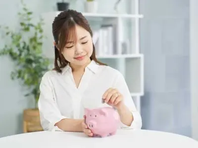 Woman in a white shirt inserting a coin into a pink piggy bank, symbolizing savings and financial planning.